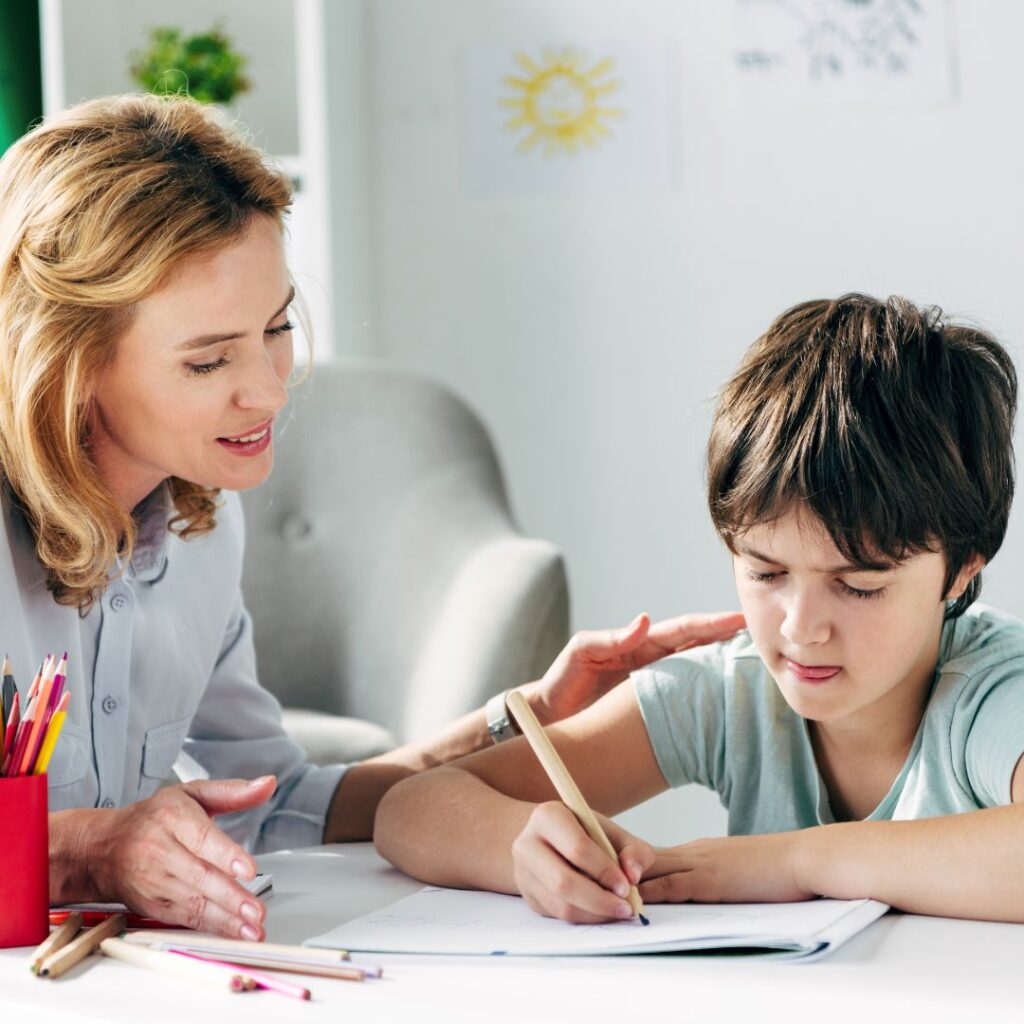 Speech therapist helping young boy with learning disabilities to write.