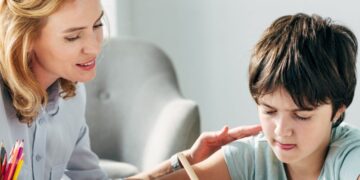 Speech therapist helping young boy with learning disabilities to write.
