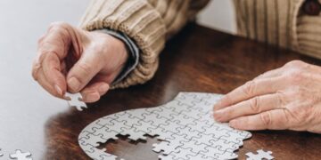 Old man with aphasia in speech, music and occupational therapy doing a jigsaw puzzle of a brain.