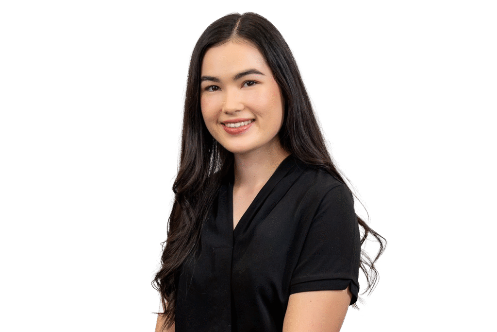 A young woman with long, straight dark hair is smiling and wearing a black short-sleeved blouse. She is posed in front of a plain white background, representing music therapy courses available on the Gold Coast.