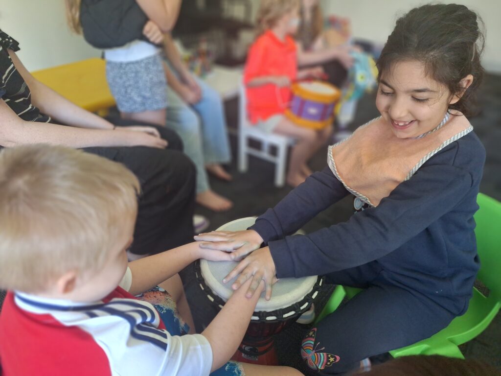 A young girl and boy playing a djembe together.