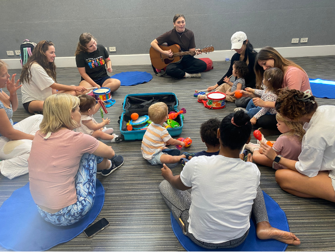 Adults and infants sitting in a circle listenig to a woman play the guitar.