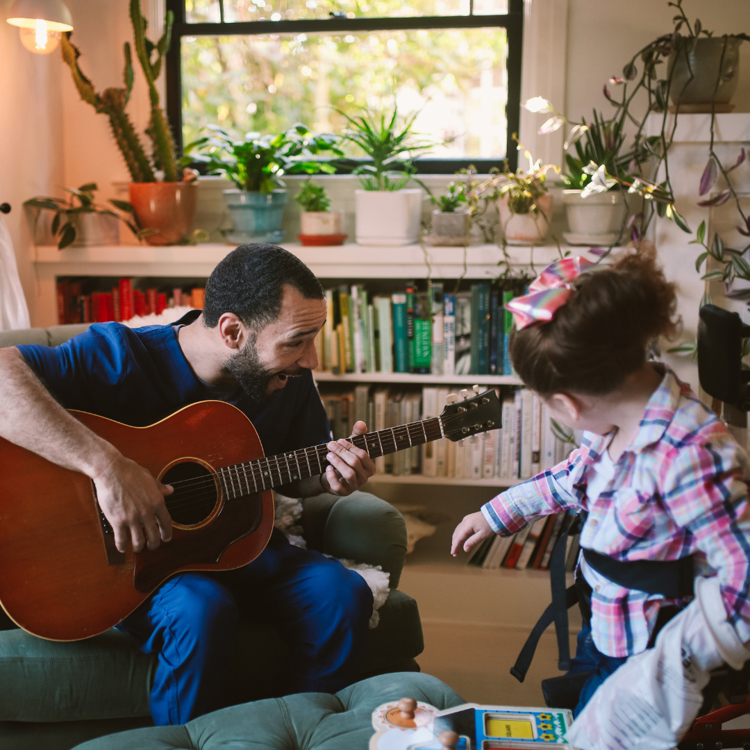 Man playing guitar to a young girl in a standing frame.