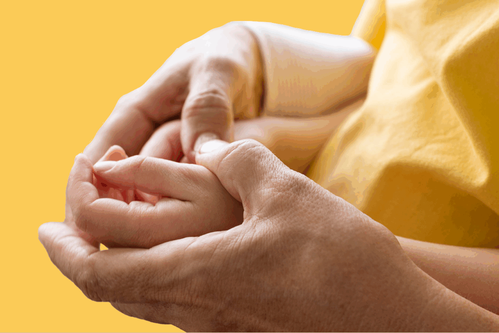 Close-up of an adult gently holding a child's hand, both in yellow clothing with a yellow background—capturing the protective care often seen in music therapy for kids on the Gold Coast.