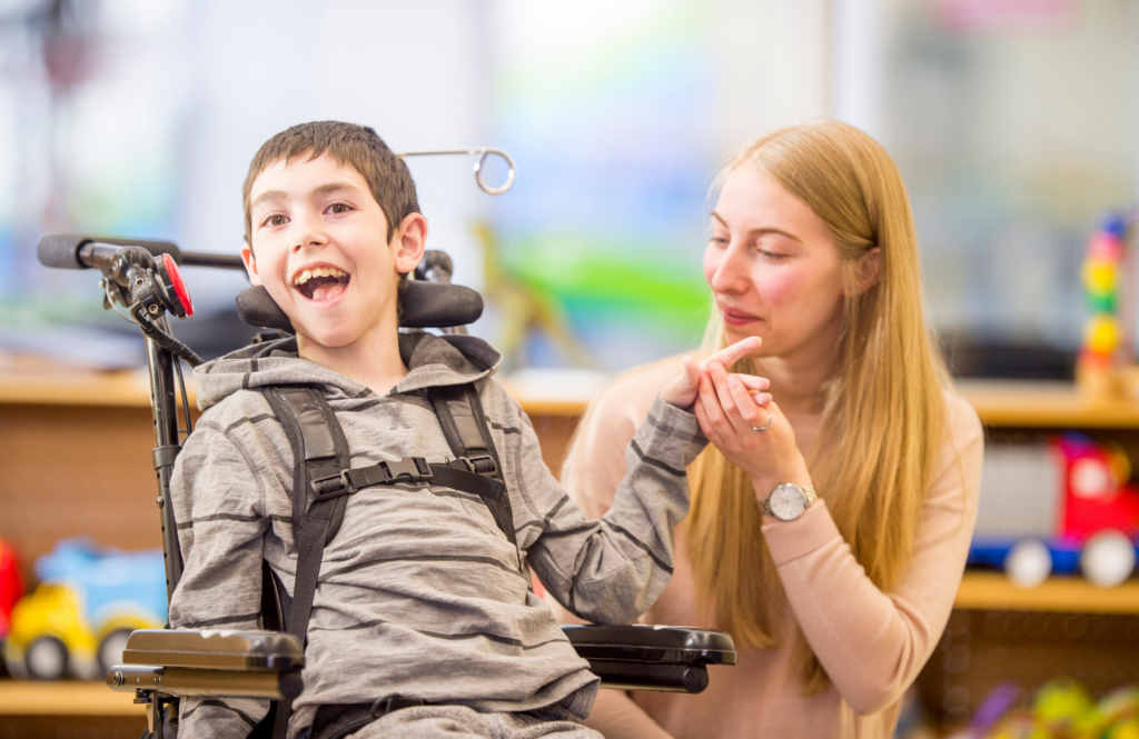 A smiling boy in a wheelchair with a woman, holding his hand.
